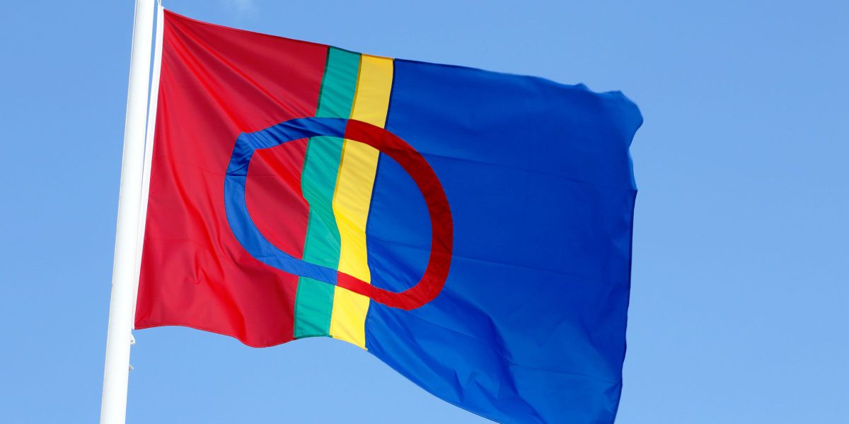 Bildet av det samiske flagget som veiver i vinden mot en blå himmel.